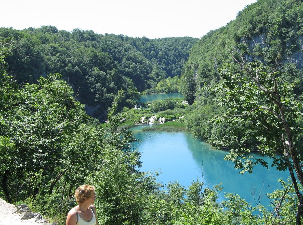 Turkooizen meren en watervallen in een weelderig groen bos, met iemand die van het uitzicht geniet.