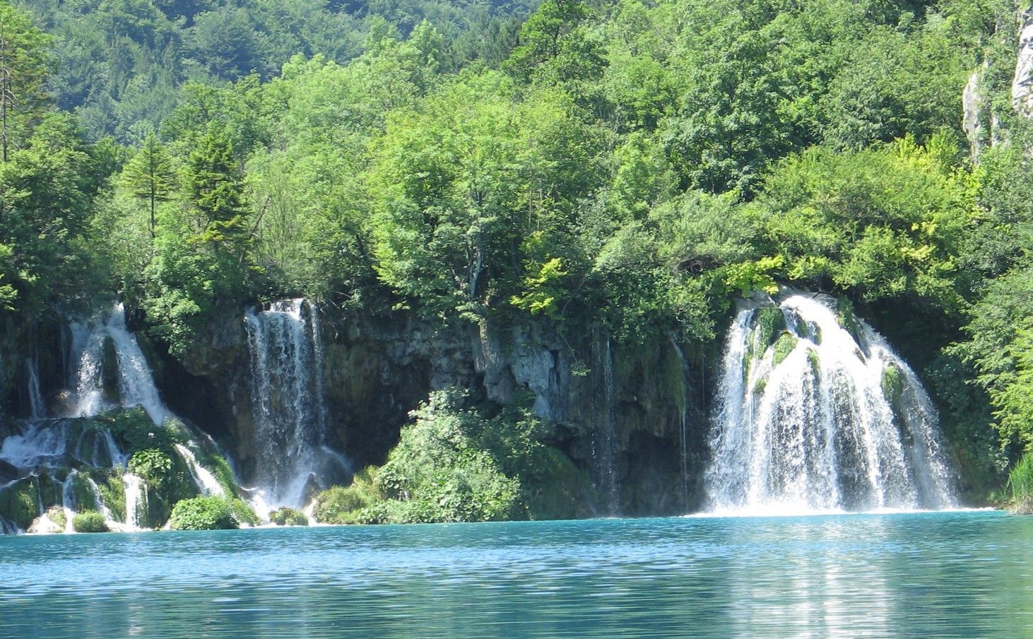 Watervallen storten zich in een turquoise meer, omgeven door weelderig groen bos.