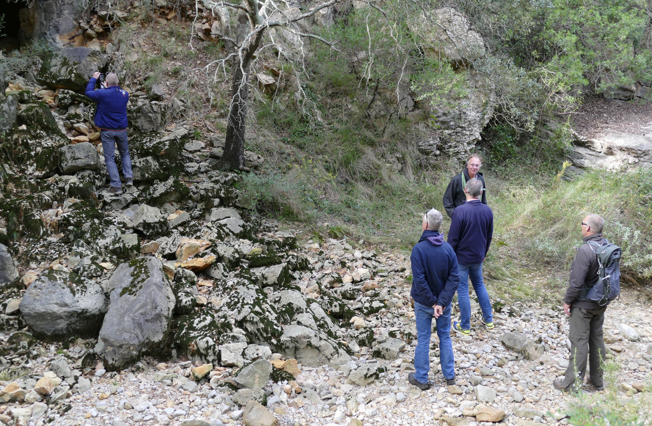 Mensen bestuderen rotsformaties in een natuurlijke omgeving, sommigen kijken omhoog naar een persoon op de rotsen.