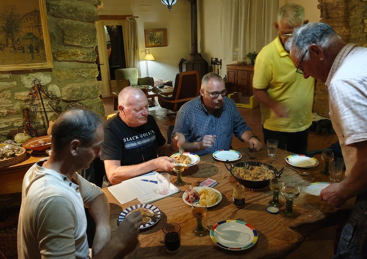 Mannen zitten aan een ronde tafel en nuttigen een maaltijd. Een warm en sfeervol interieur met een ongedwongen ambiance.