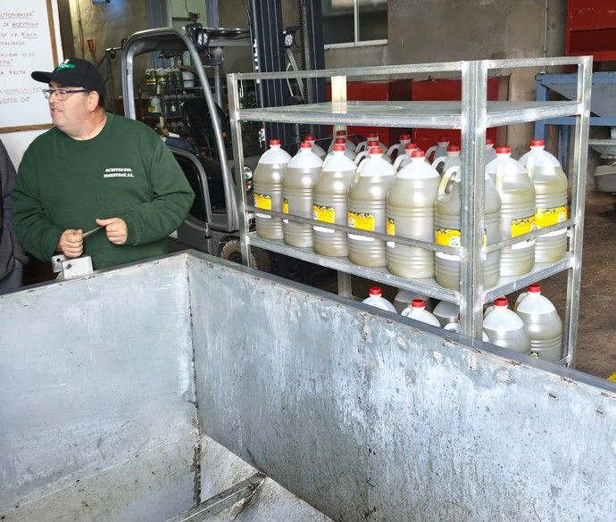 Man in groen shirt bij een schap met grote flessen. Industriële omgeving met heftruck en grote tank.