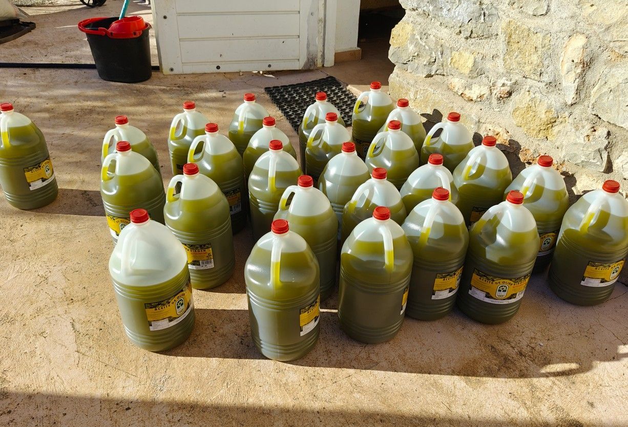 Olijfolie in grote plastic kannen met rode deksels, buiten op een zonnige dag.