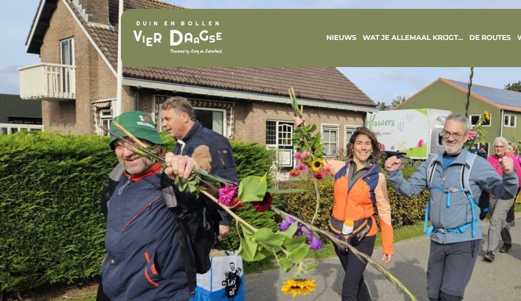 Een groep lachende mensen met bloemen in hun handen loopt over straat, met een gebouw op de achtergrond.
