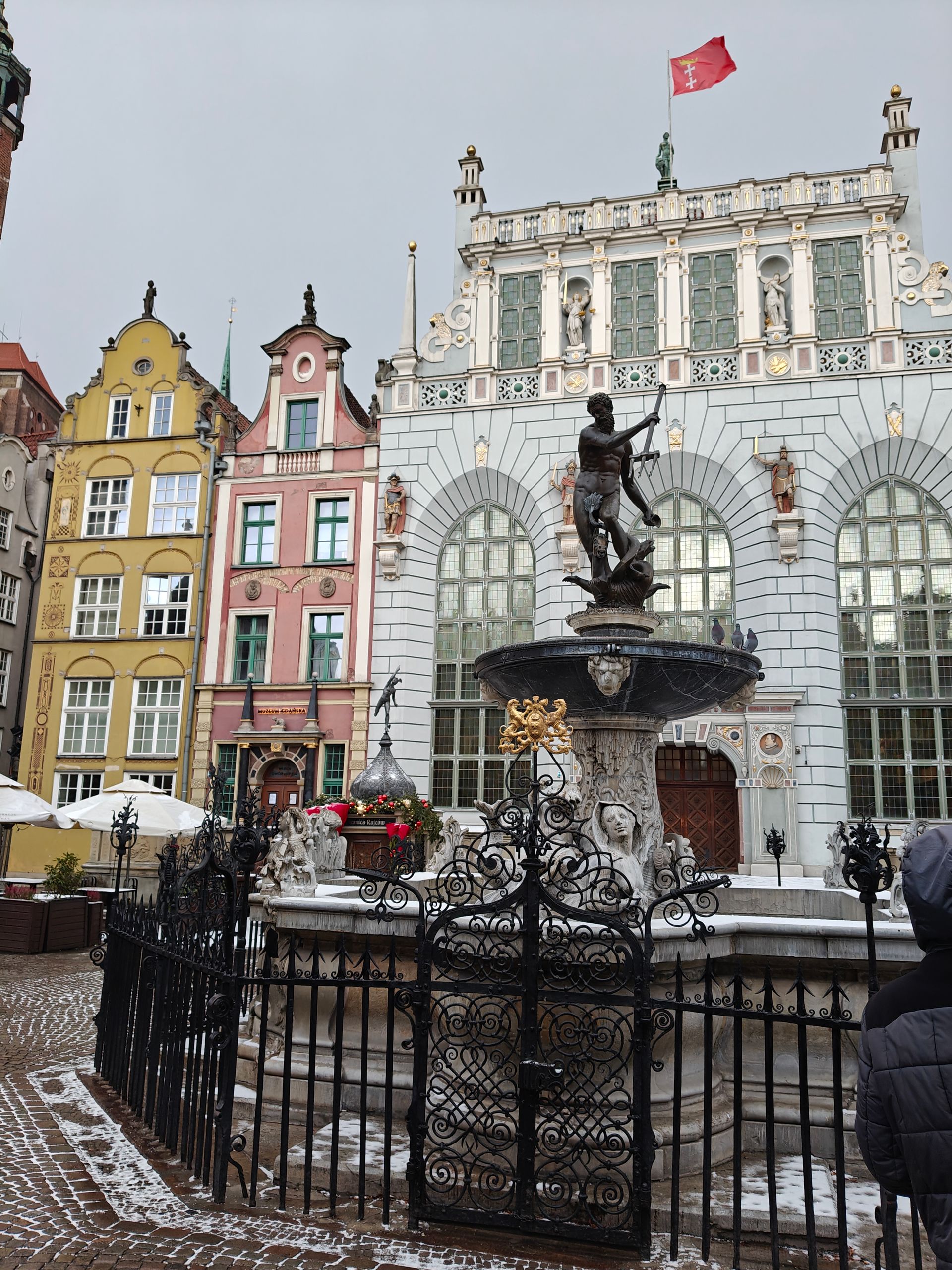 Fontein met standbeeld van Neptunus voor sierlijke gebouwen. Besneeuwd plein, rode vlag wapperend.