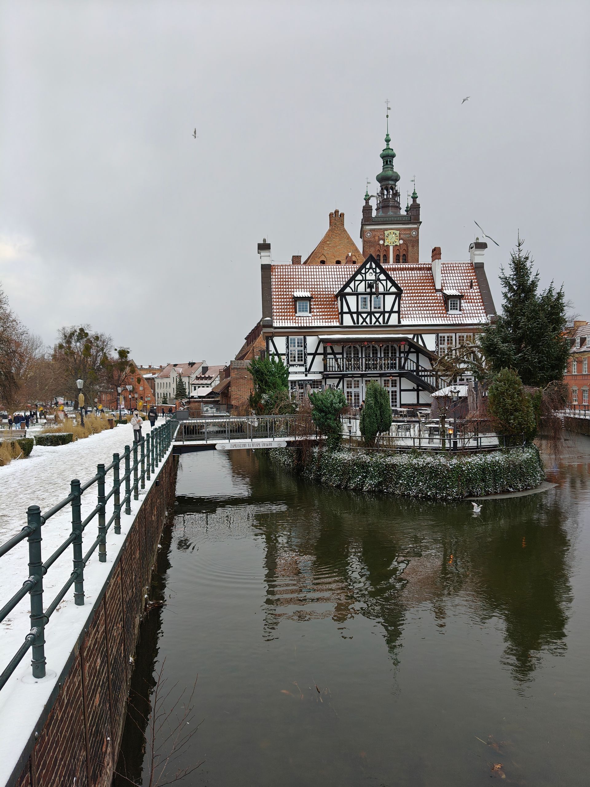 Besneeuwd uitzicht op een gebouw met een klokkentoren en een weerspiegeling in het water. Zwart-wit houten frame.