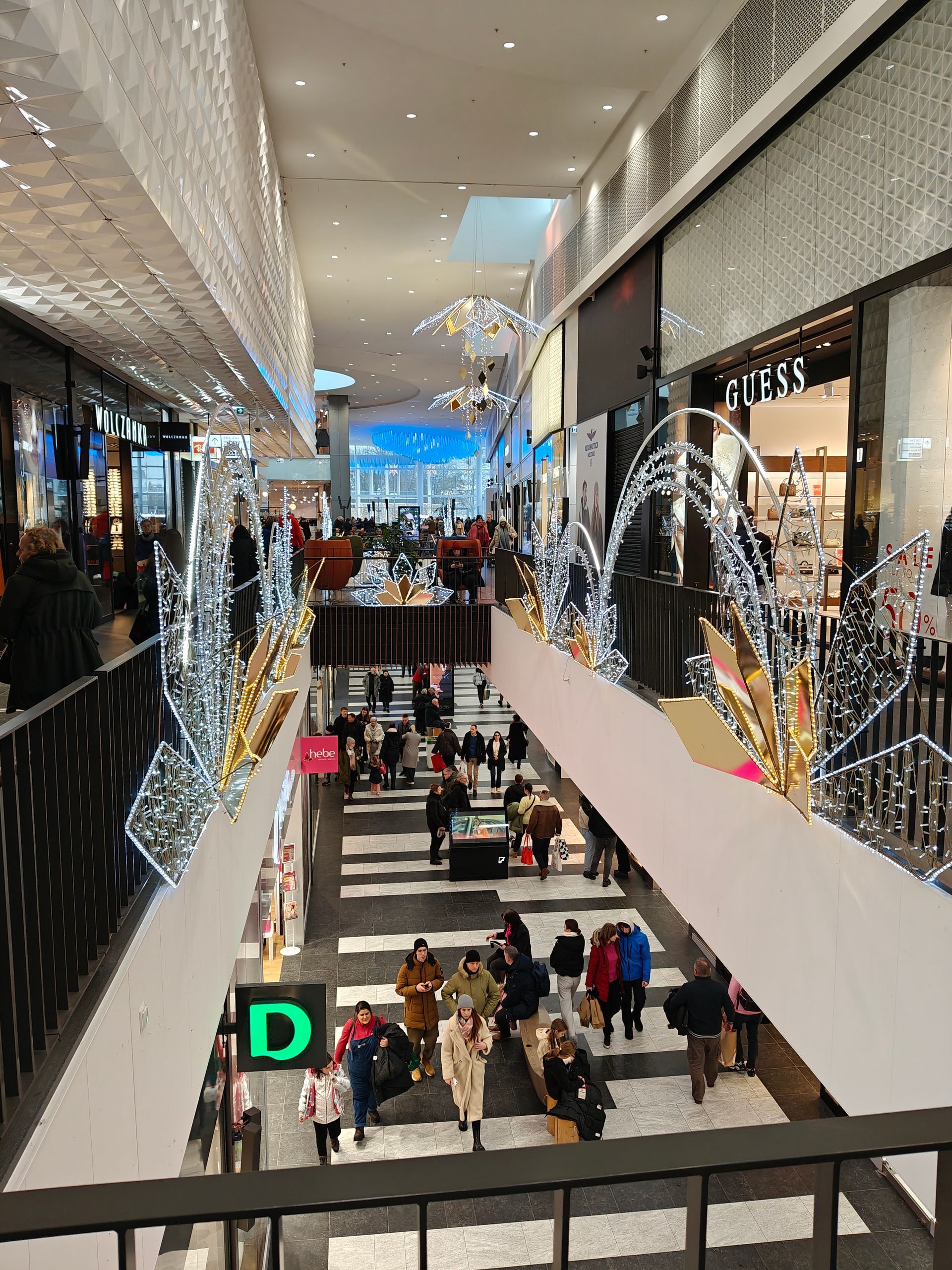 Interieur van een winkelcentrum vol winkelend publiek. Kerstversieringen hangen aan de bovenverdieping.