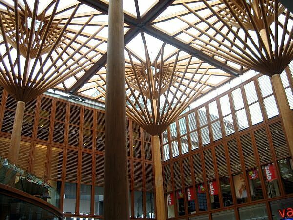 Interieur van een modern atrium met een houten rasterdak en hoge glazen wanden.