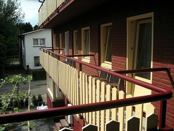 Balkon van een appartement met rode balustrade en gele panelen naast een bakstenen gebouw