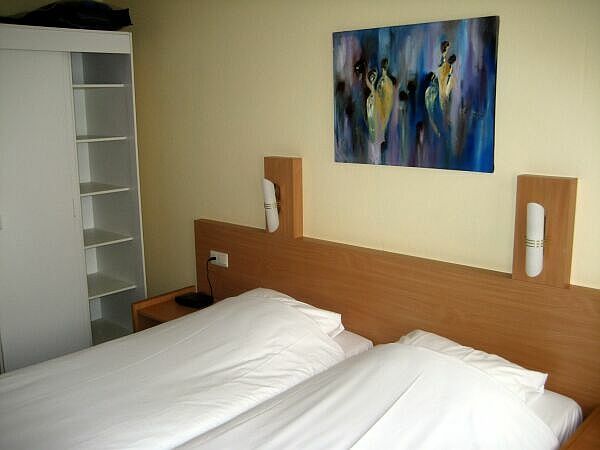 Hotelkamer met twee onopgemaakte eenpersoonsbedden, houten hoofdeinden en een muurschildering erboven.