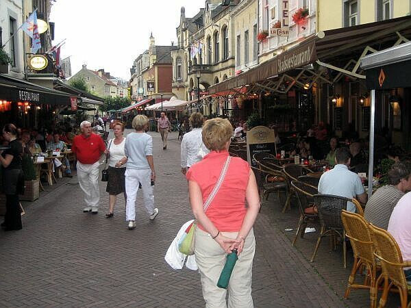 Een drukke voetgangersstraat met terrasjes en historische gebouwen aan weerszijden.