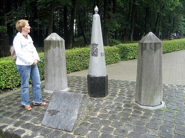 Een persoon staat naast stenen monumenten en een scheefstaande plaquette in een bosrijk park.