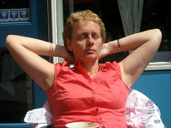 Persoon in een rood mouwloos shirt ligt buiten in de zon met de handen achter het hoofd.