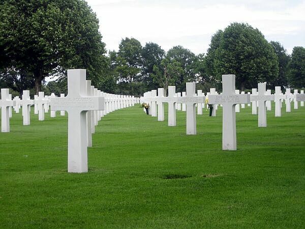 Rijen witte kruizen op een groen gazon van een begraafplaats onder een bewolkte hemel.