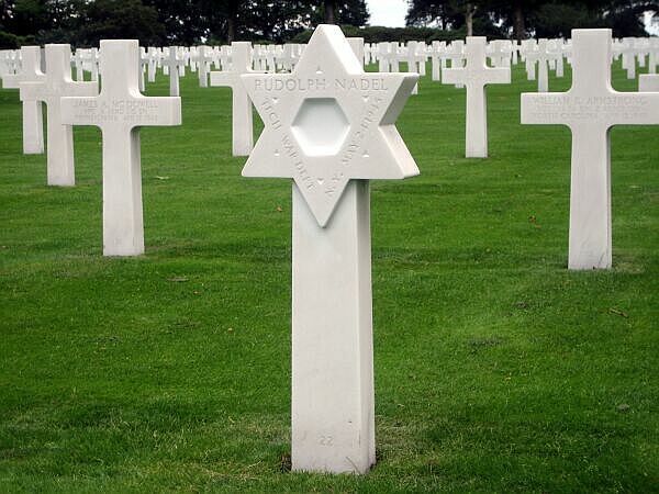 Witte militaire grafstenen op een groene begraafplaats, waaronder een grafsteen met een Davidster op de voorgrond.