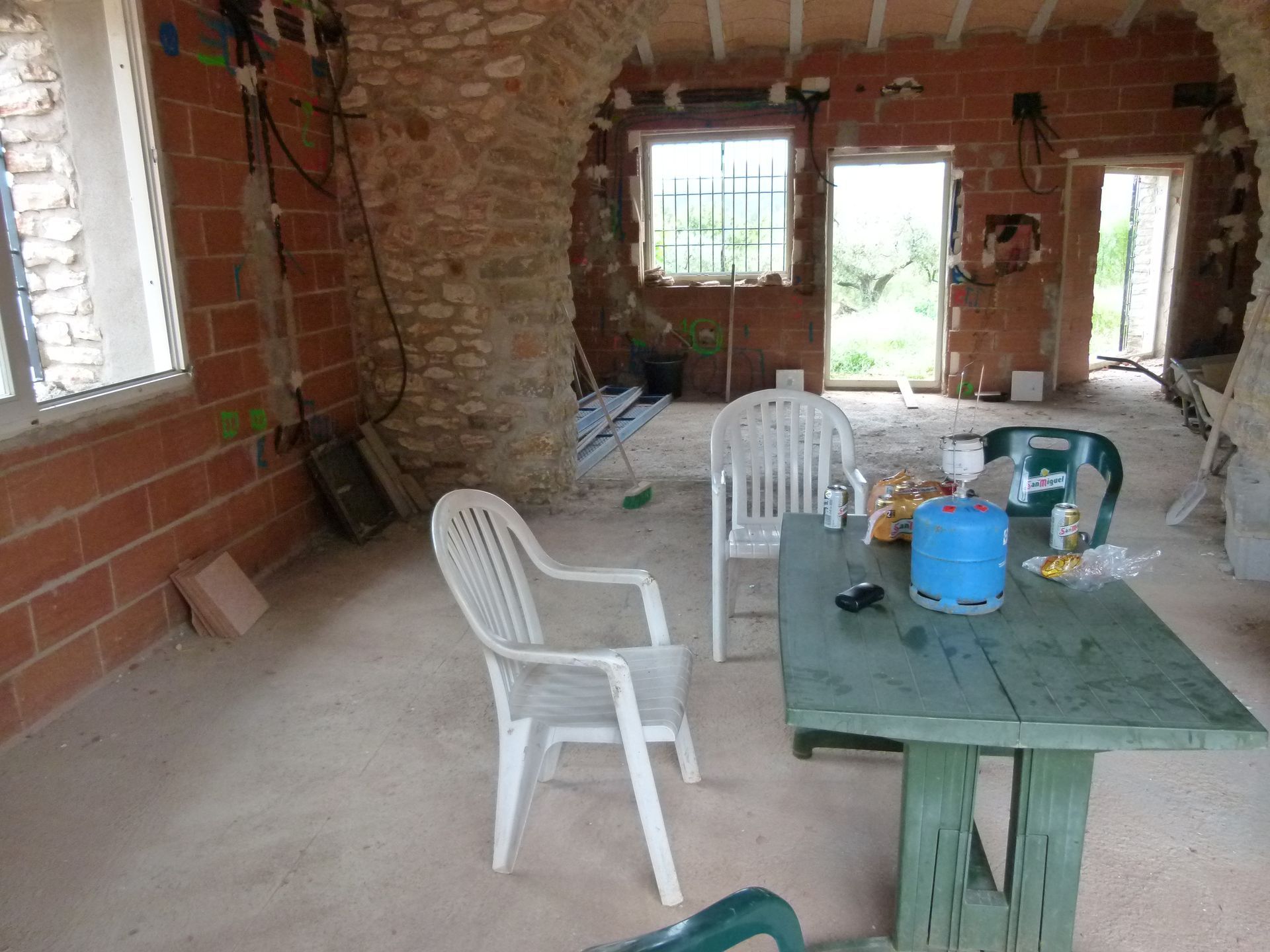 Interieur in aanbouw met stenen bogen, ramen en een tafel met stoelen.