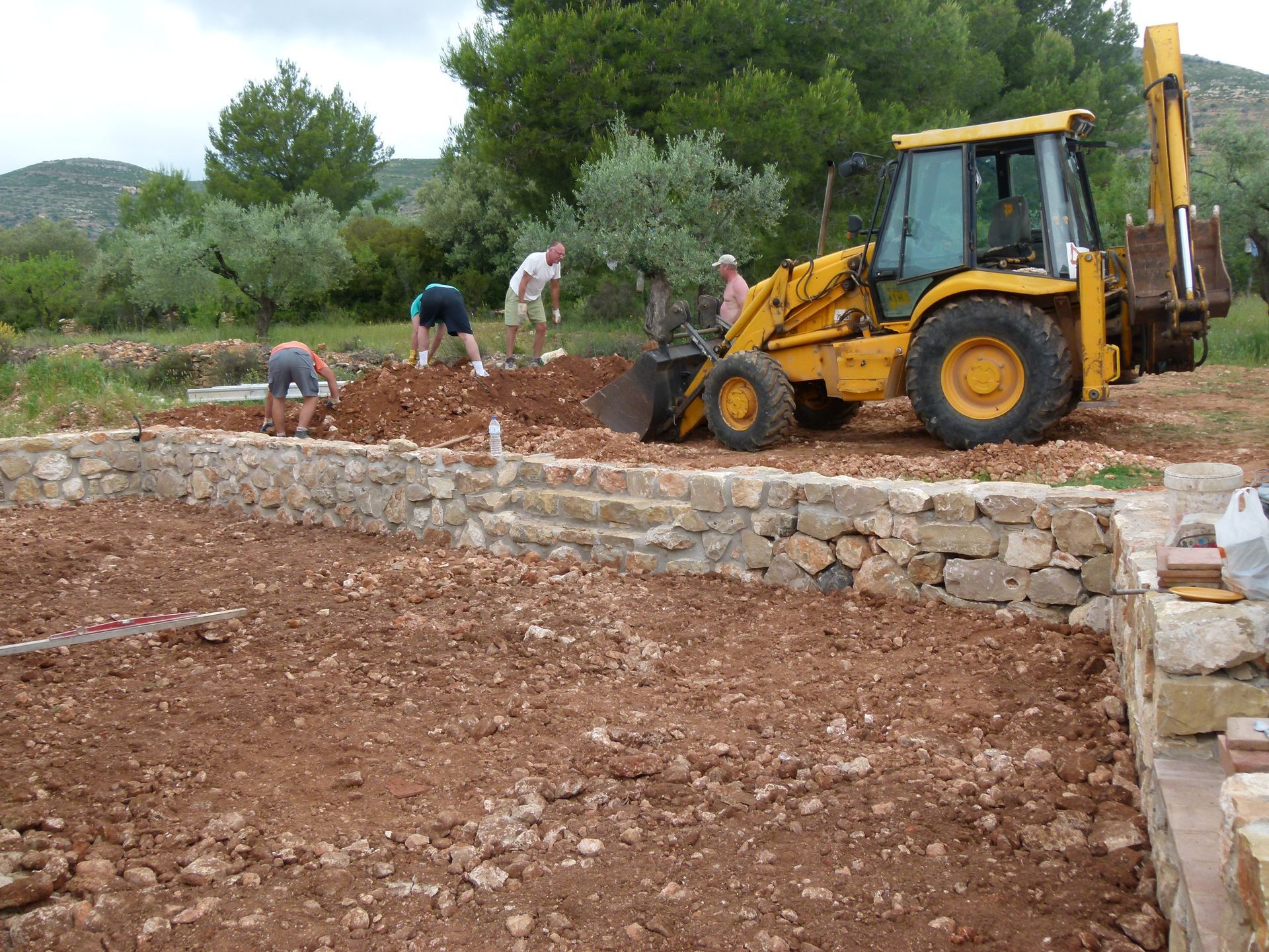 Bouwplaats: graafmachine en arbeiders bouwen een fundering van stenen. Buiten, bruine aarde.