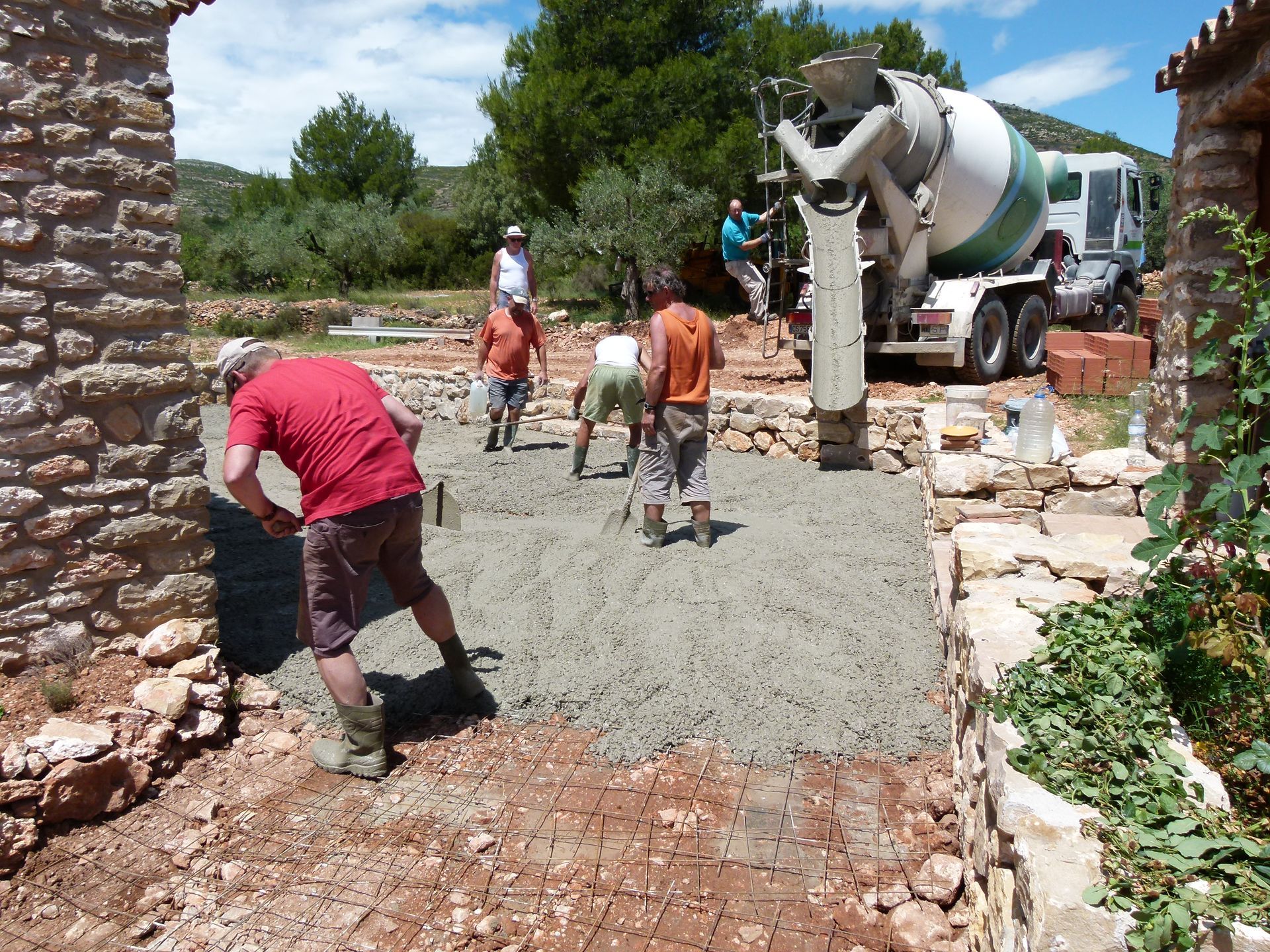 Arbeiders storten beton vanuit een vrachtwagen en egaliseren het op een bouwterrein met stenen muren.