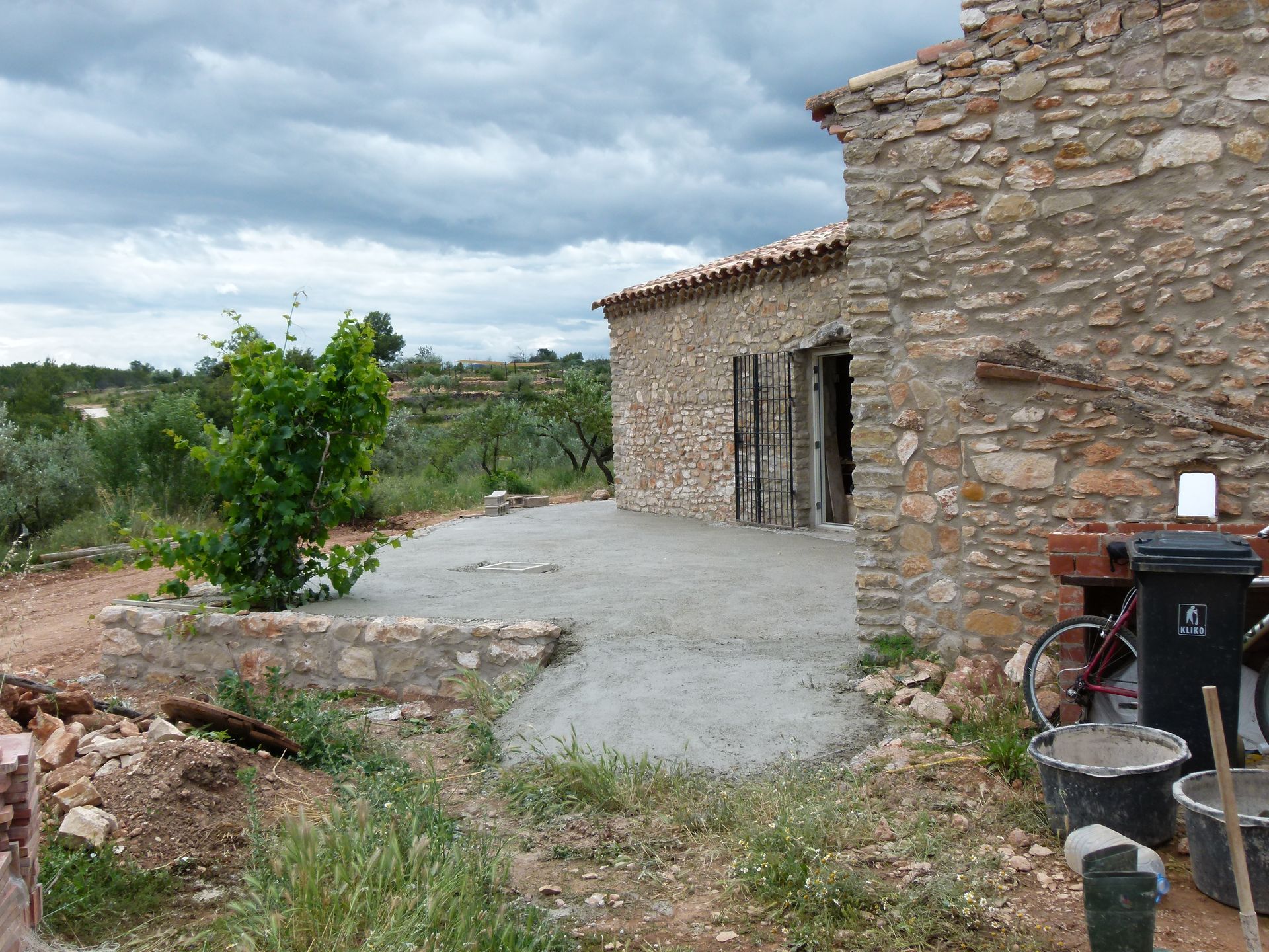 Stenen huis met een pas aangelegd betonnen terras. Bewolkte lucht.