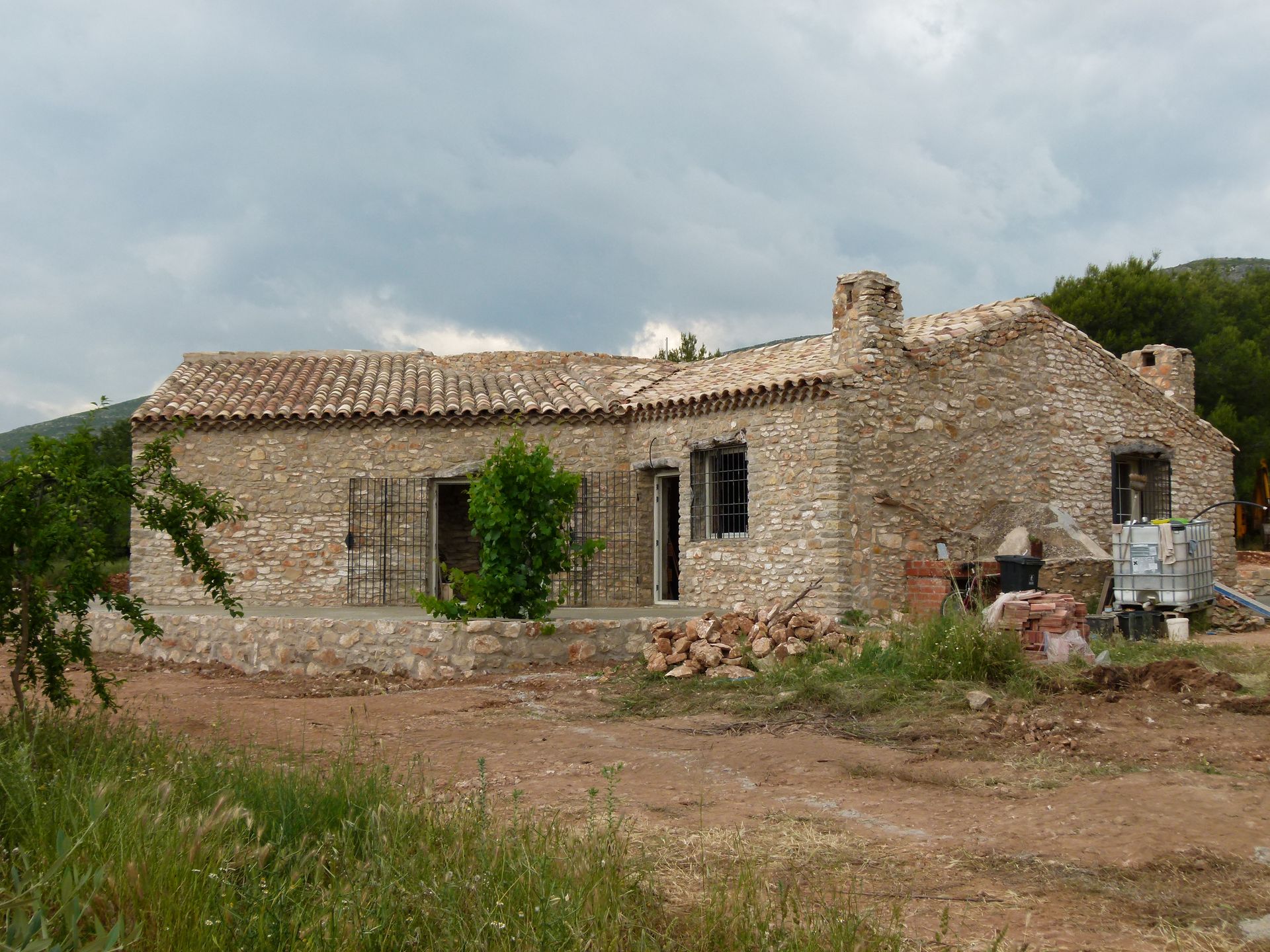Stenen huis in aanbouw met pannendak, luiken en schoorsteen.