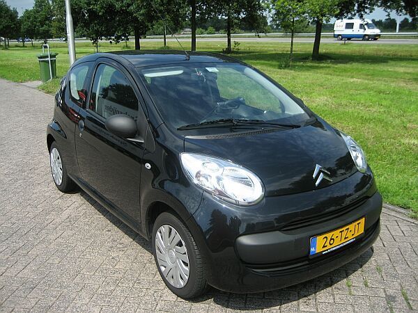 Een Citroën C1 staat geparkeerd op een verharde weg langs een grasveld.