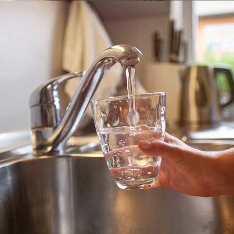 pouring glass of fresh water from tap in kitchen