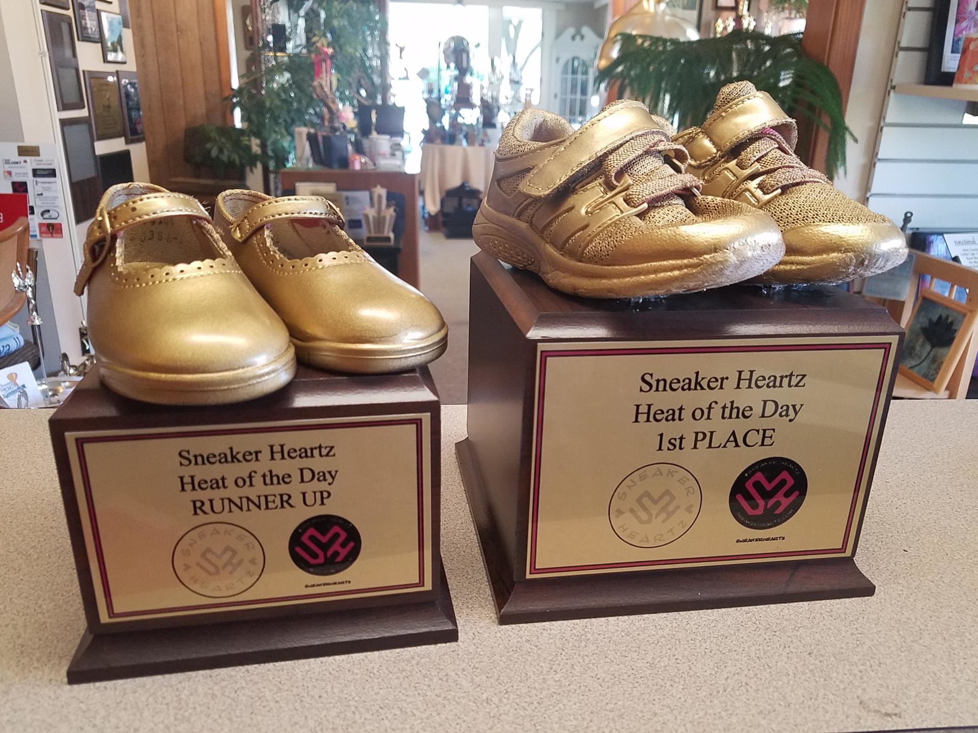 A pair of gold shoes sitting on top of a plaque that says sneaker heart heat of the day runner up