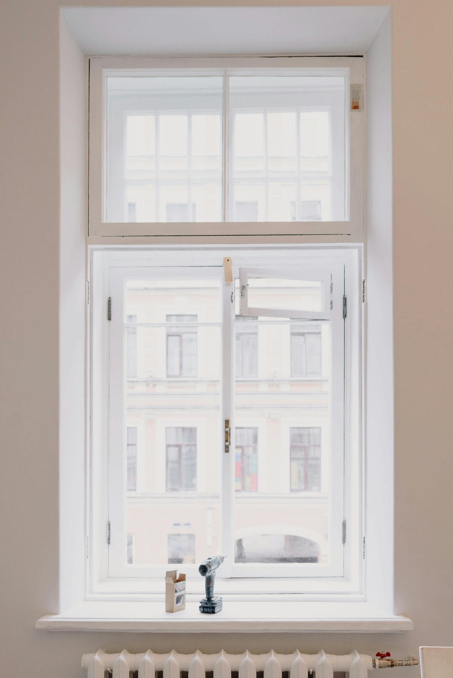 A white window with a drill on the window sill.