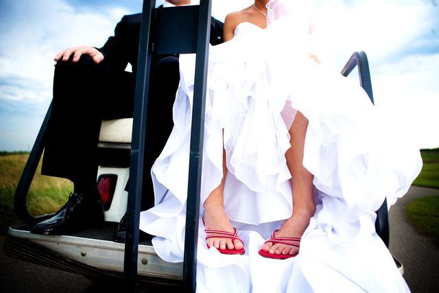 A bride and groom are sitting on the back of a golf cart