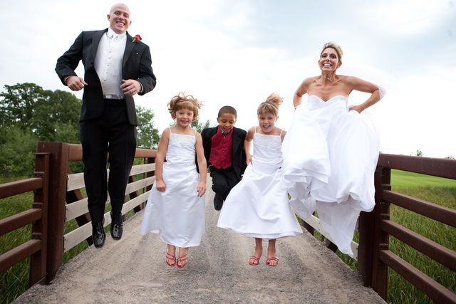 A bride and groom are jumping over a bridge with their children