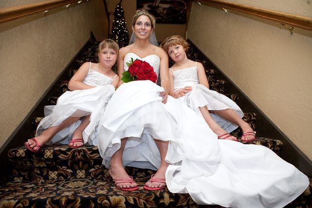 A bride and her two flower girls are sitting on the stairs