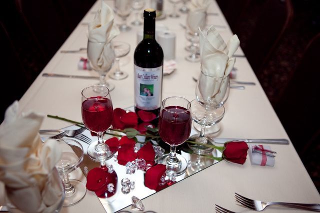 A bottle of wine sits on a table with glasses and roses