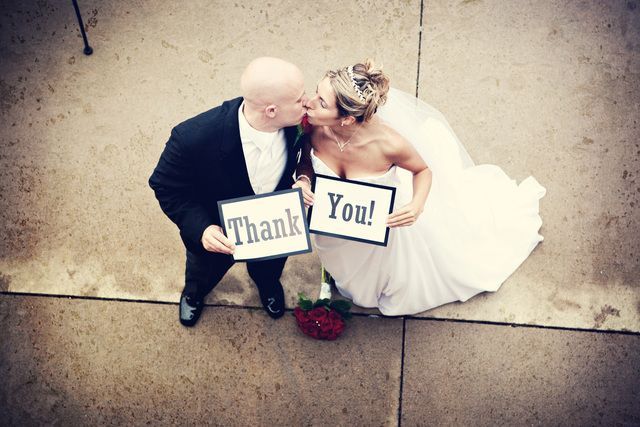 A bride and groom kissing while holding thank you signs