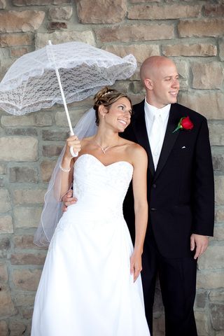 A bride and groom are standing next to each other holding an umbrella.