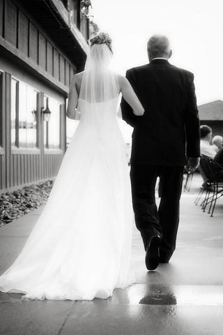 A black and white photo of a bride walking down the aisle with her father.