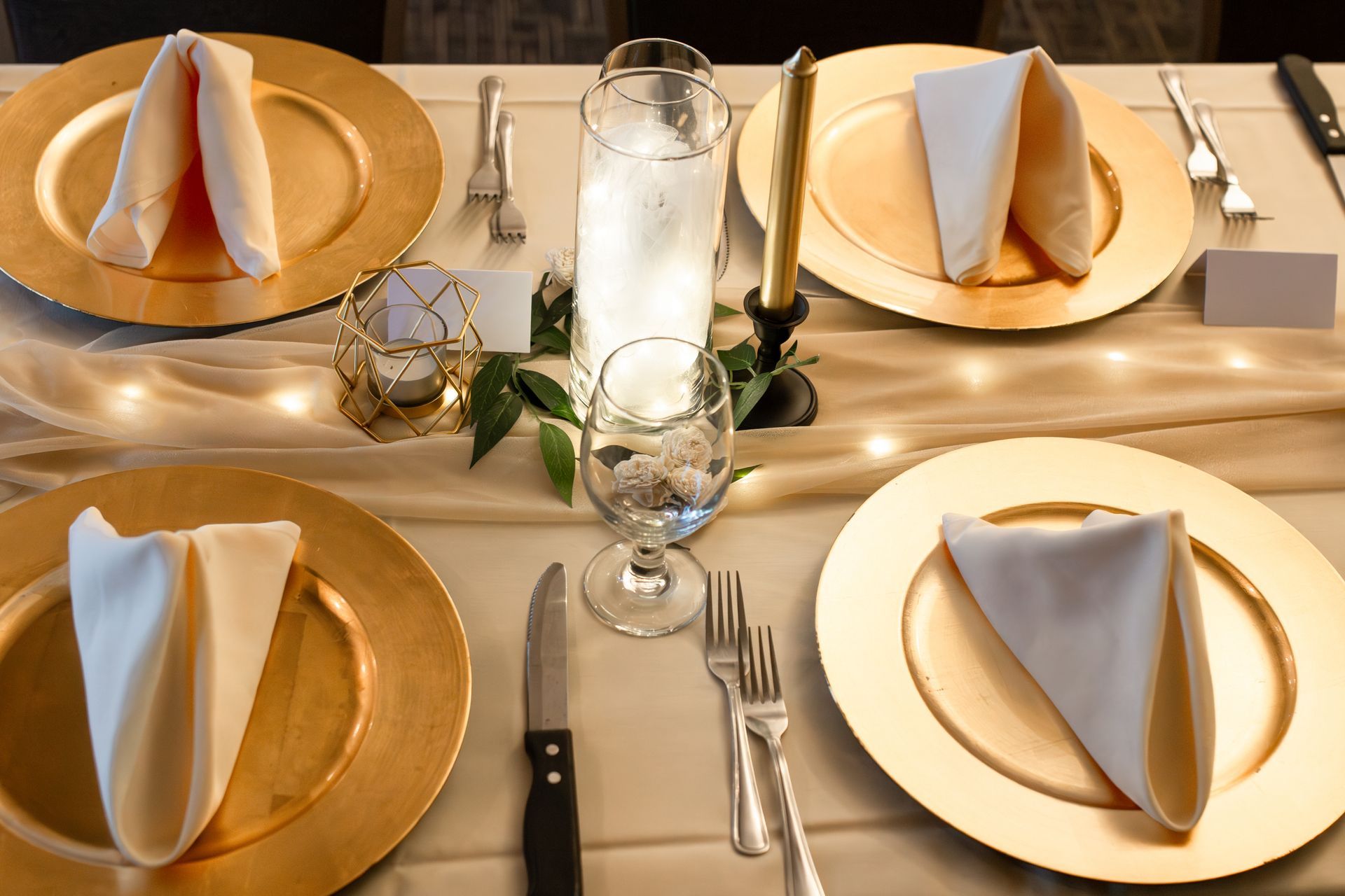 A table set for a wedding reception with gold plates and white napkins.