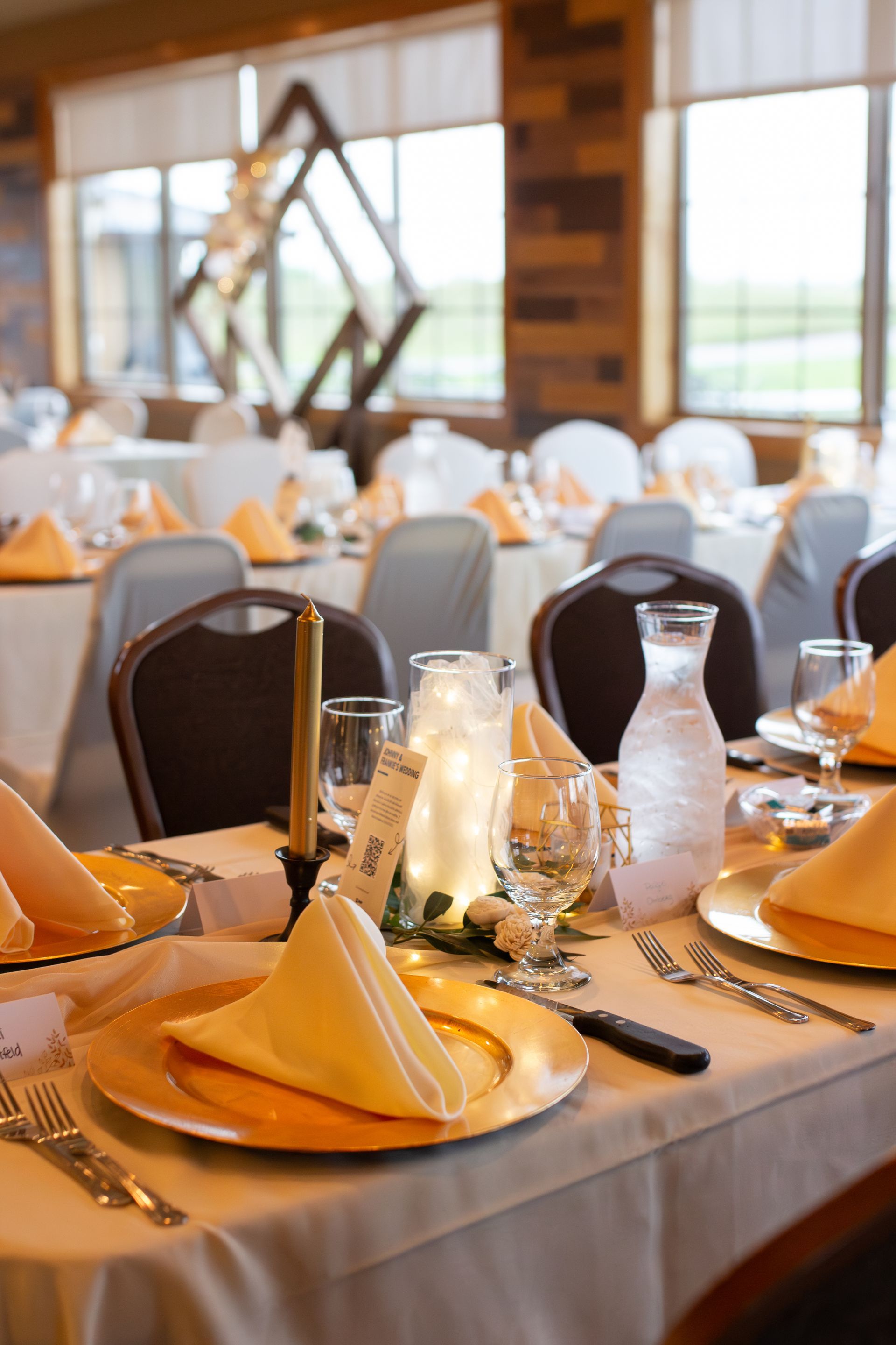 A table set for a wedding reception with plates , napkins , candles and glasses.