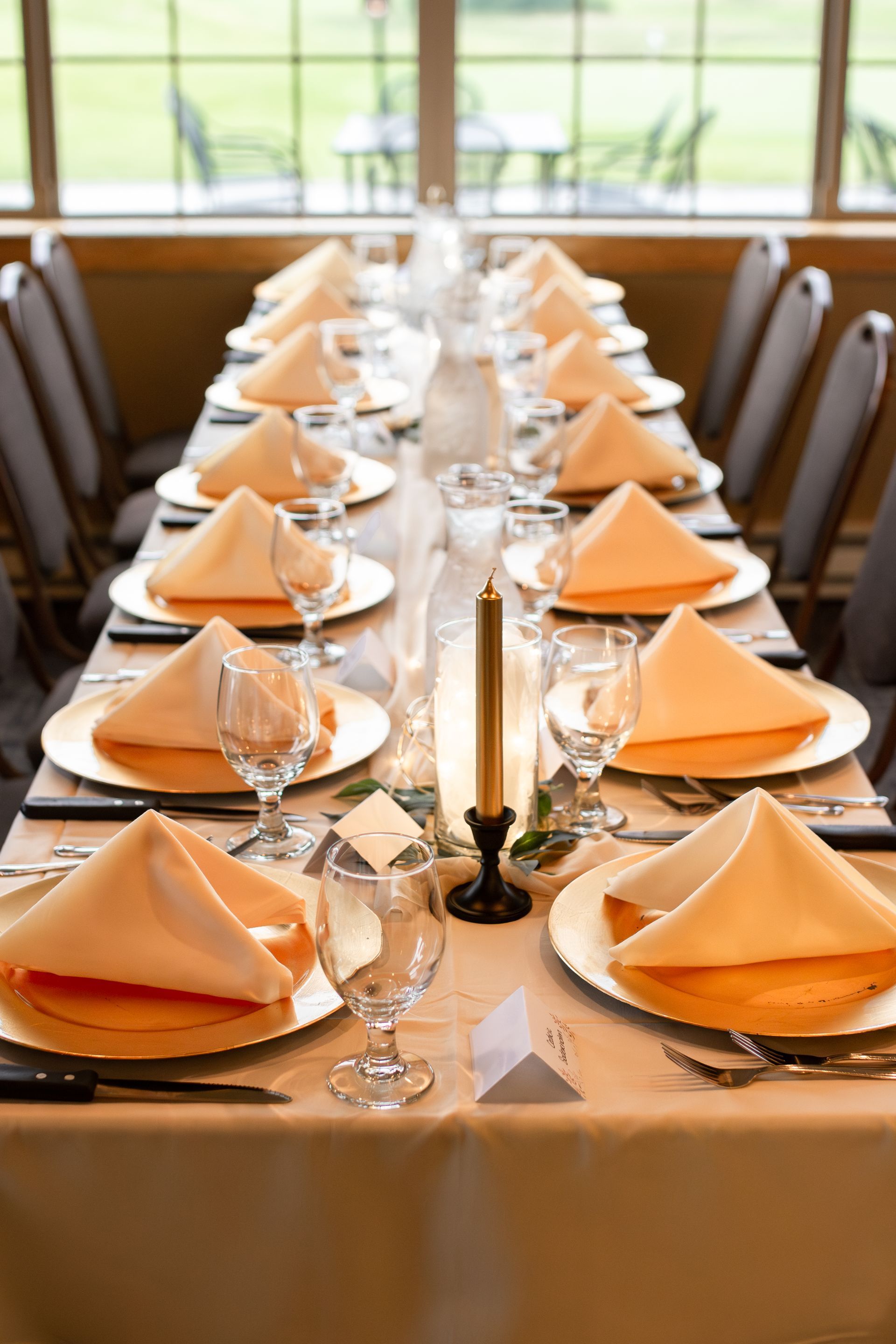 A long table with plates , glasses , napkins and a candle.