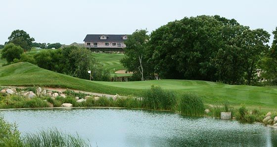 Golf course with green grass, water, and a building on a hill.