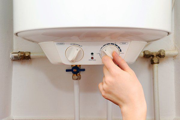 A person's hand carefully adjusts the temperature dial of a boiler.