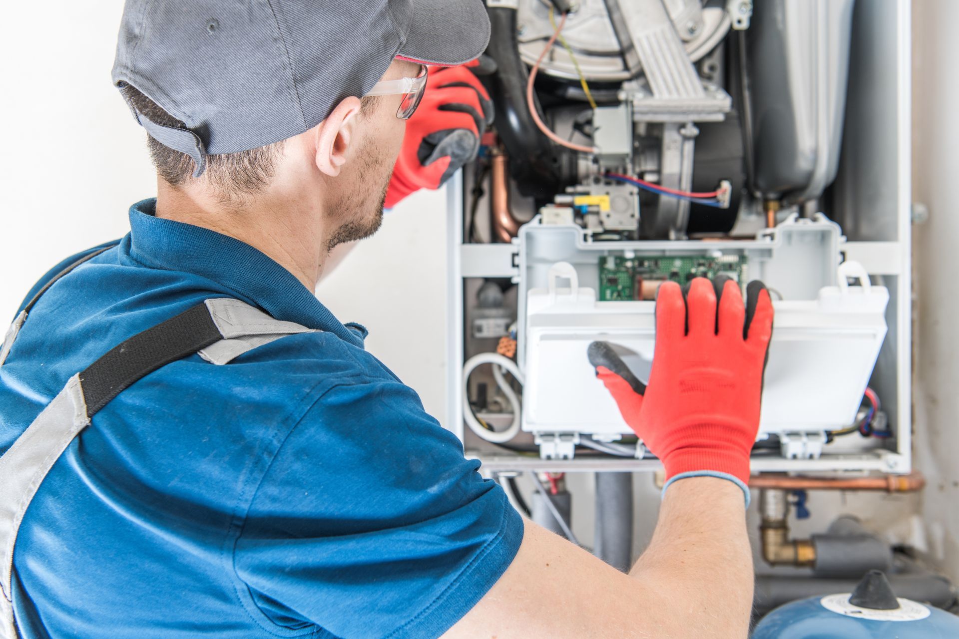 An expert technician in a blue uniform performing furnace repair, carefully inspecting and repairing the internal components of a residential furnace.