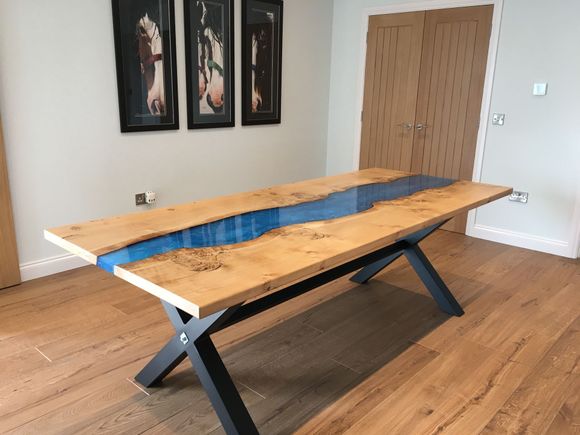 A burry oak river table with metallic blue resin and  black metal X-frame legs.