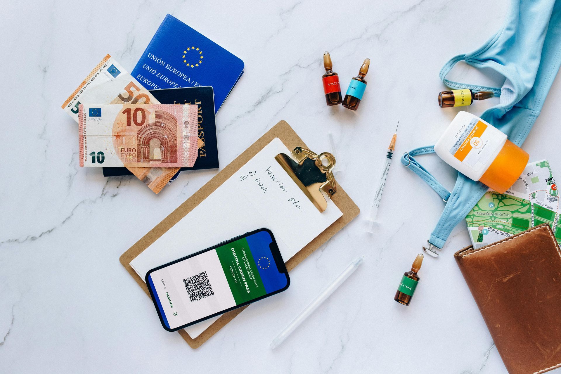 Travel essentials: passport, cash, phone, sunscreen, bag, and notebook on a white surface.