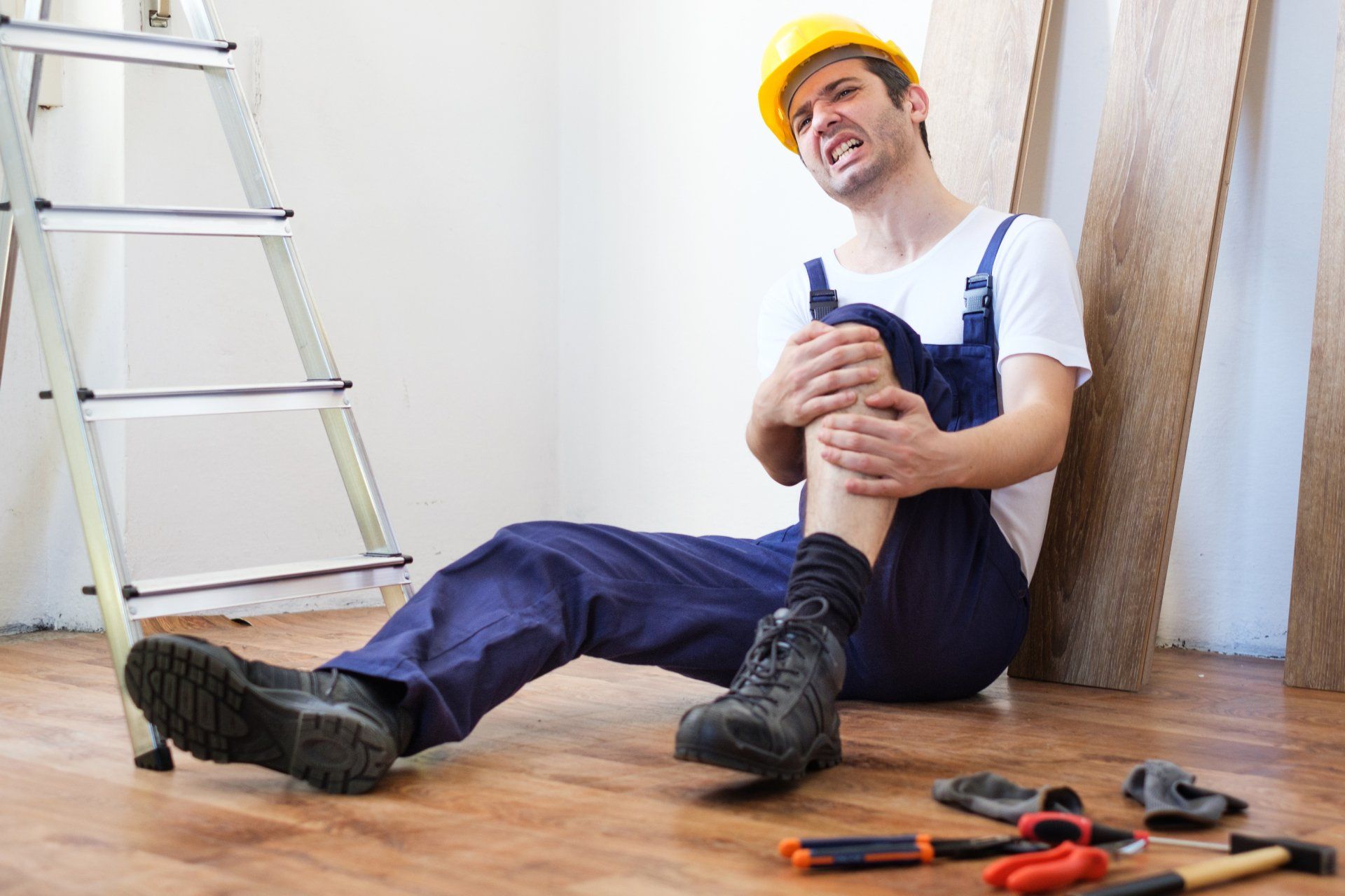 A man is sitting on the floor with his knee in pain.