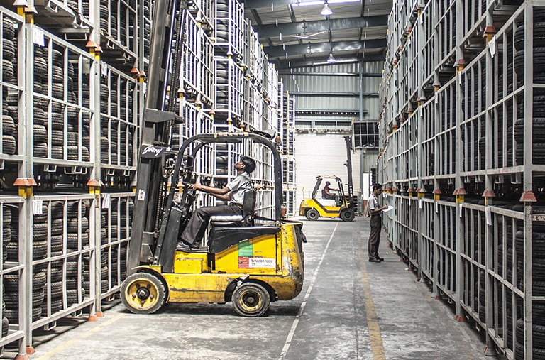 A man is driving a forklift in a warehouse filled with lots of tires.