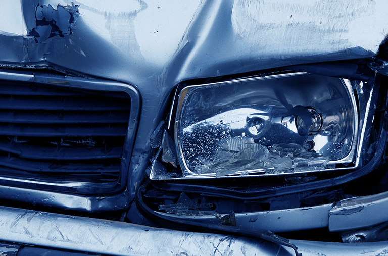 A close up of a damaged car with a broken headlight.