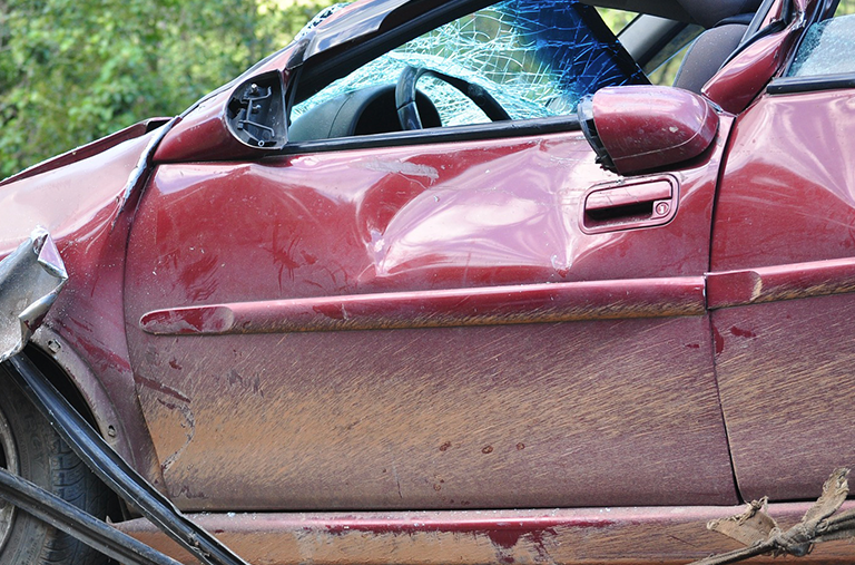 A red car with a broken windshield is sitting on the side of the road.