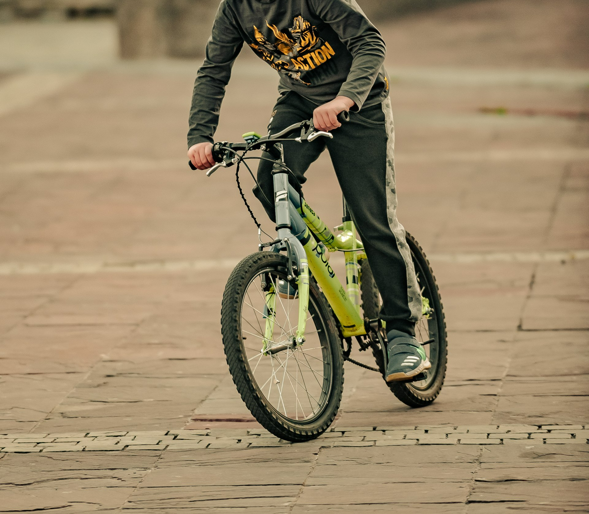 A man is riding a bicycle on a brick sidewalk wearing a shirt that says strong