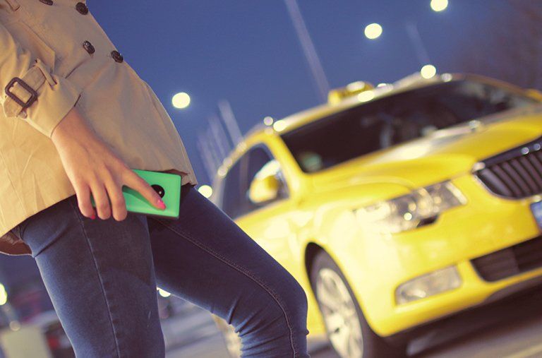 A woman is standing in front of a yellow taxi holding a cell phone.