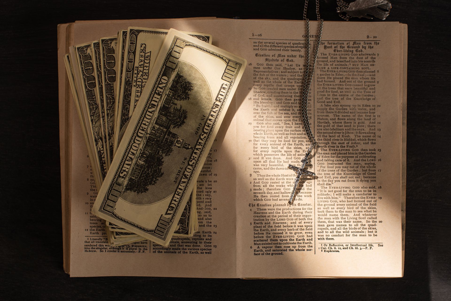 Stacks of $100 bills on open book with a cross necklace.