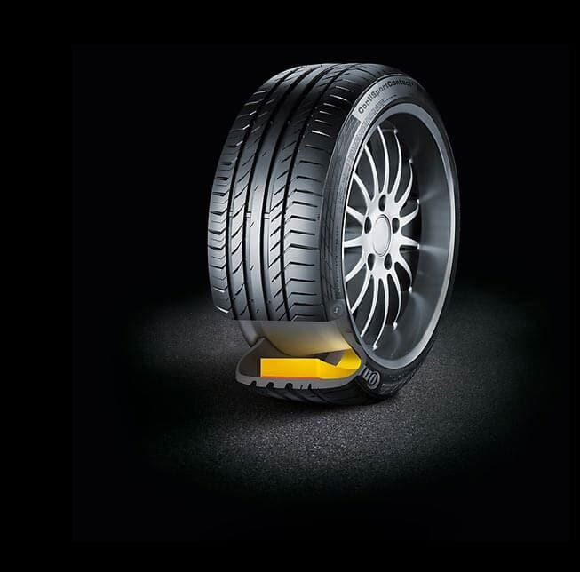 Corte transversal de un neumático de automóvil sobre una superficie negra, mostrando una inserción amarilla para mantener la forma.